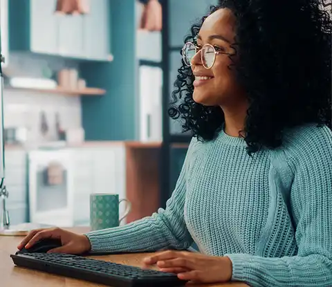 Imagen de una estudiante de las maestrías online de UNAPEC, sonriendo al ingresar a la plataforma de estudios desde la computadora de su hogar.